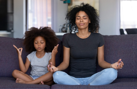 Photo credit: fizkes/iStock/Getty Images. Mother and young daughter doing yoga together at home on their couch
