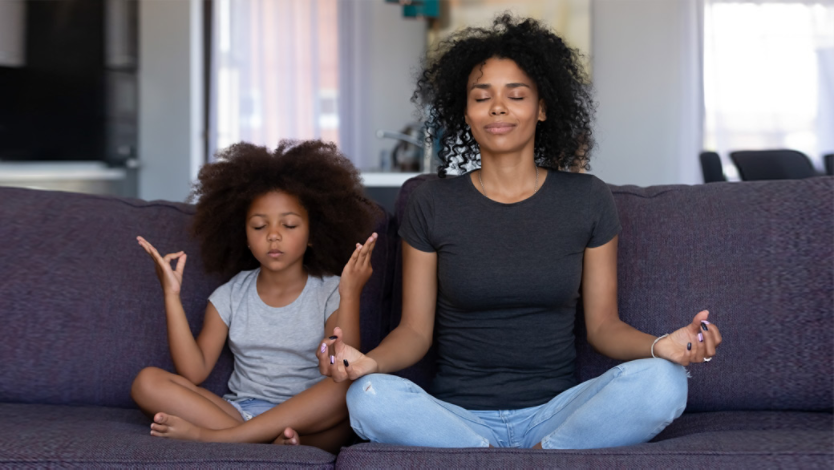 Mother and daughter doing yoga together sitting on their couch