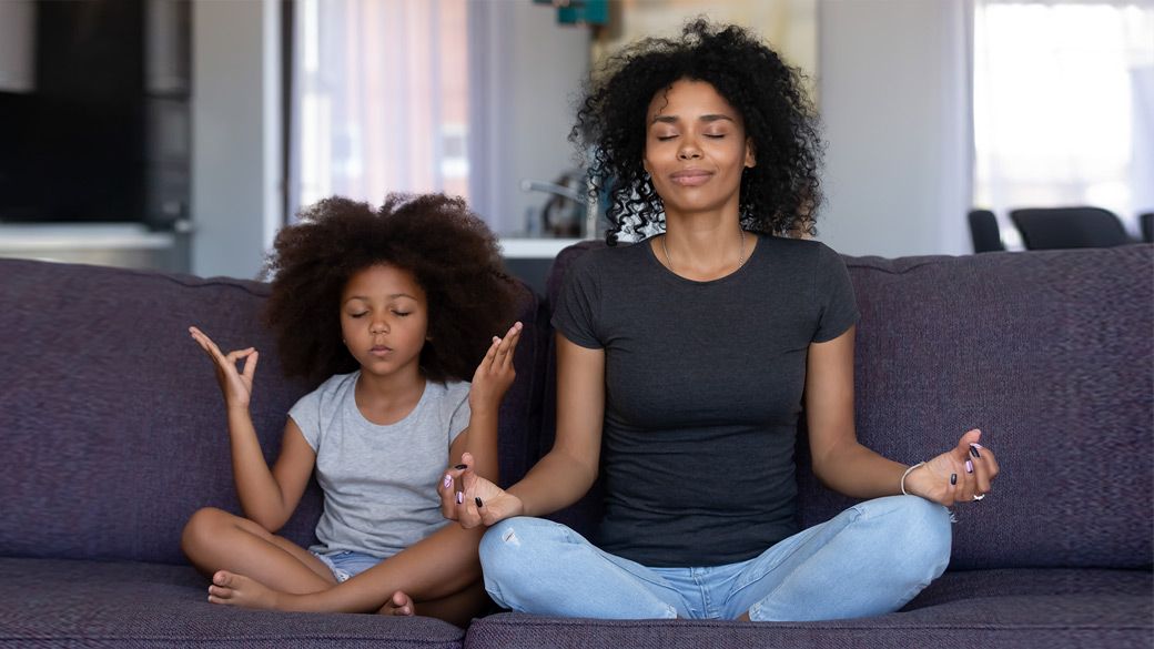 Mother and young daughter doing yoga together at home on their couch