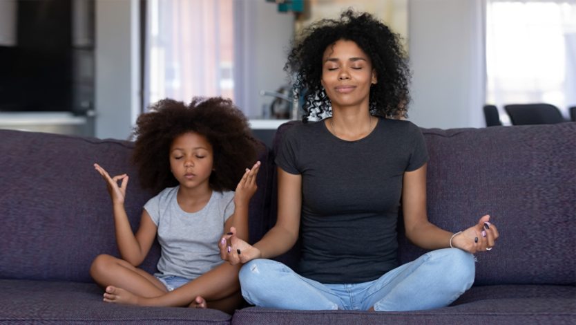 Mother and daughter doing yoga together sitting on their couch