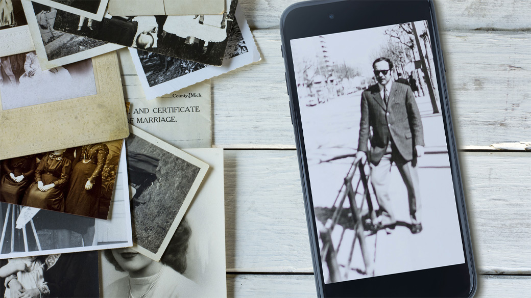 Pile of old black and white photos next to a mobile phone showing a scan of an old photo.