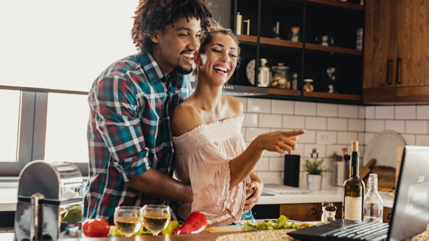 Photo credit: blackCAT/E+/Getty Images. Smiling man and woman look at recipe on Windows 11 laptop while cooking together in kitchen