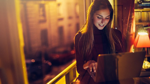 Crédit photo : filadendron/E+/Getty Images. Une femme travaille chez elle sur un ordinateur portable dans une pièce faiblement éclairée