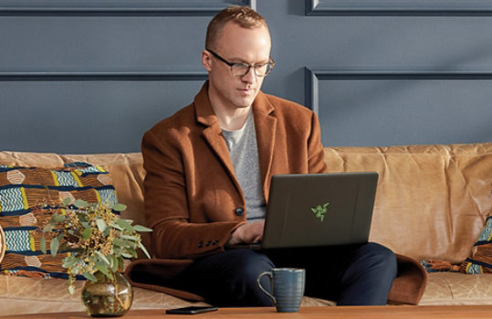 A man sits on a couch using a Razer laptop computer