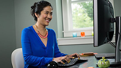 Woman sitting at desk smiling at monitor while typing on her keyboard