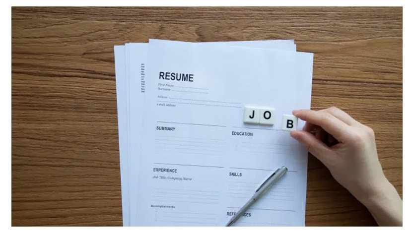 A photograph of a resume with a hand spelling out JOB in Scrabble tiles