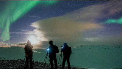 Three people photographing an aurora borealis.