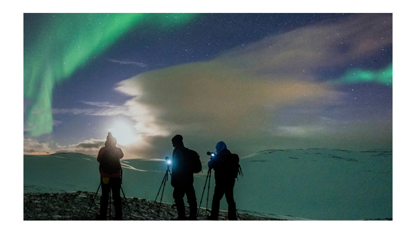 Three people photographing an aurora borealis.