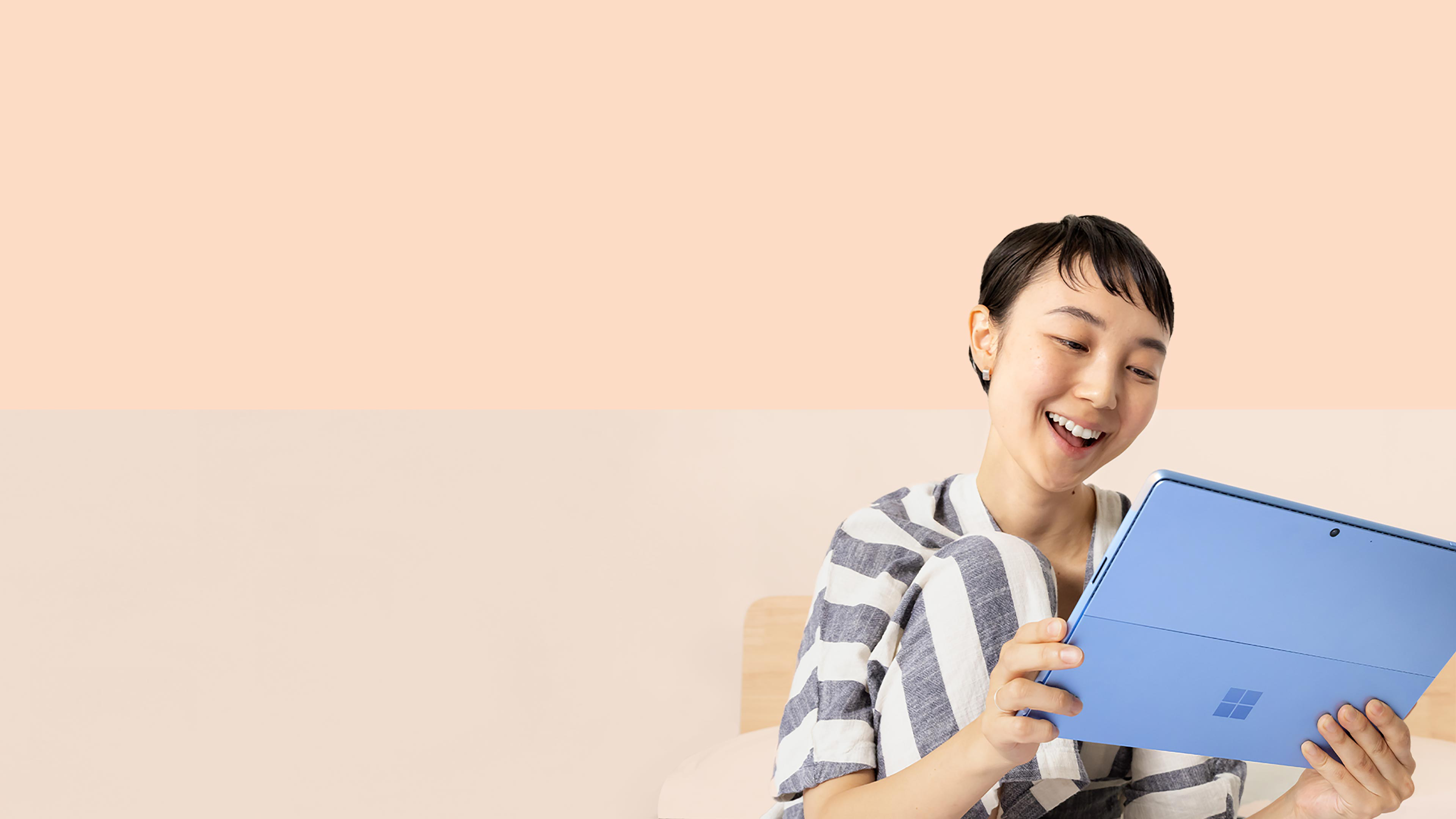 A woman smiles at her Surface Pro 9 in Sapphire while holding a Surface Slim Pen 2.