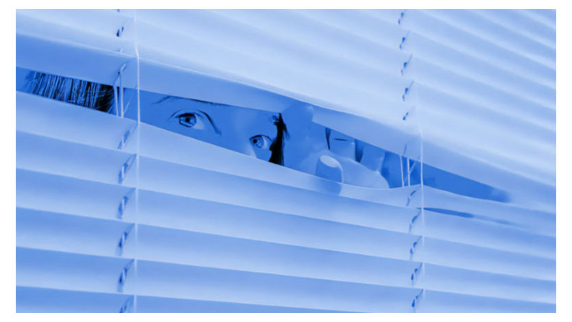 A blue-toned photograph of a person peeking through miniblinds