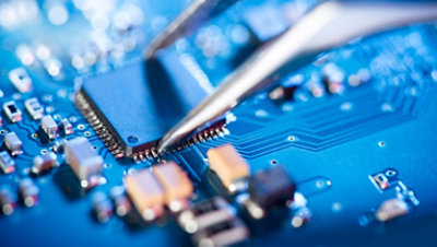 Close-up of an electronic technician holding tweezers and assembling a circuit board.