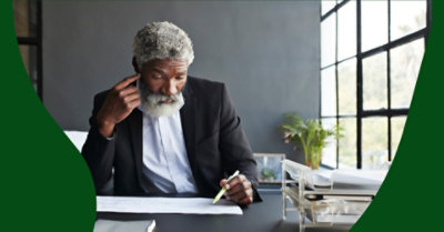 Egy íróasztalnál dolgozó férfi egy papírlappal és egy tollal.