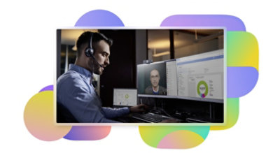A person sitting at their desk wearing a headset participating in a Teams video call being displayed on one screen and looking at data on another.
