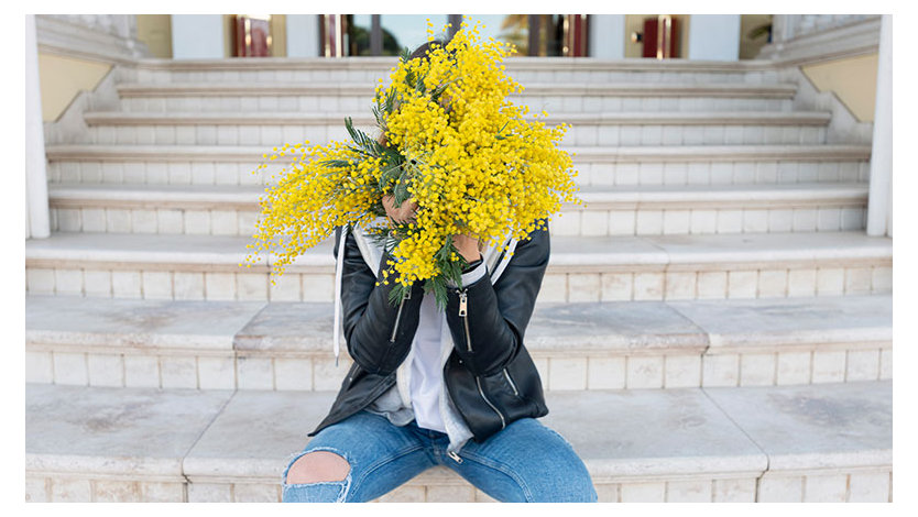 Person sitting on stairstep, with a bouquet of flowers hiding their face