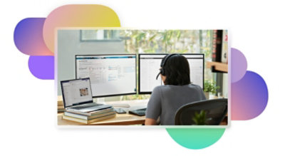 A person wearing a headset working at their desk with a laptop connected to two monitors and a keyboard.