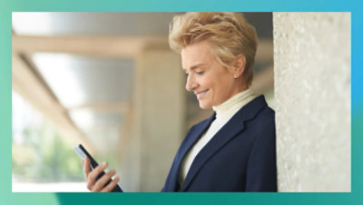 Osoba koja se smeje i gleda u mobilni telefon u ruci.