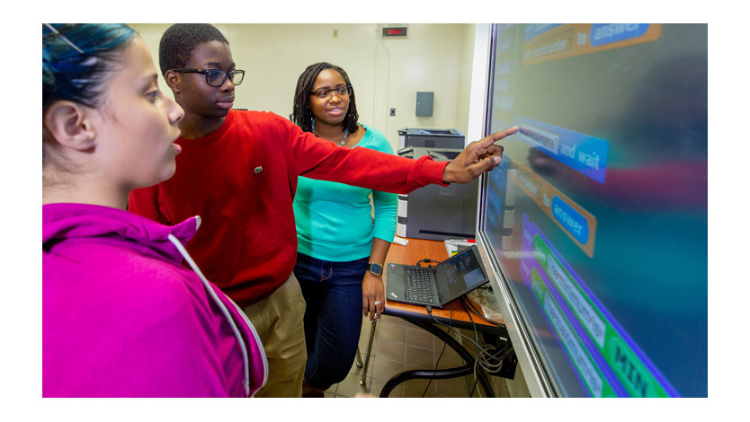 Three young people using a large touchscreen in a classroom