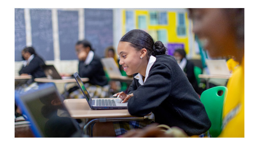 Smiling young girl at school using a laptop computer.