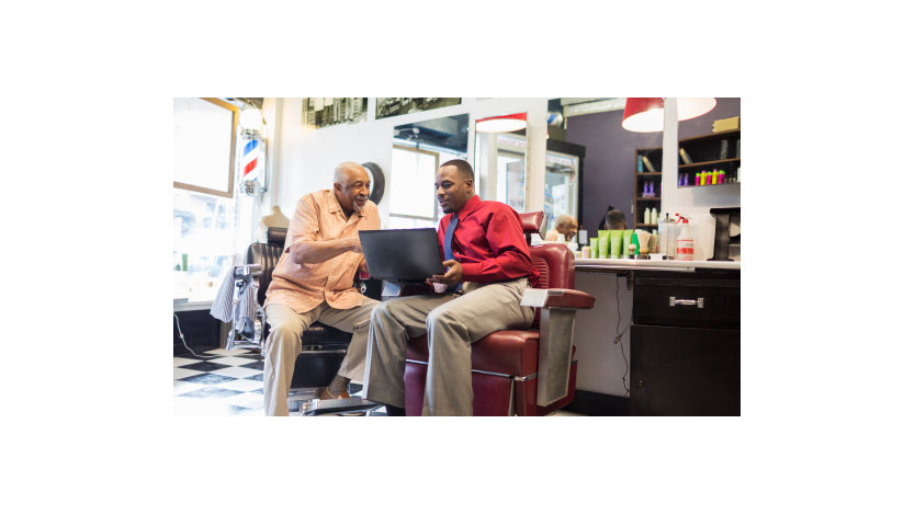 Black businessmen using laptop in retro barbershop.