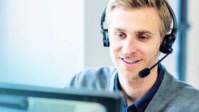 Osoba nosi slušalice sa mikrofonom i radi za stolom.