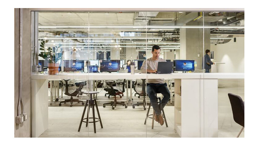 A man sits at a long, narrow table with several computers on it.