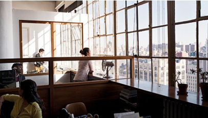 Woman looking out large window of office building overlooking a city