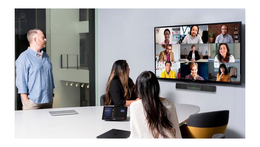 A group of Microsoft employees conduct a Microsoft Teams remote meeting on a large, mounted display.