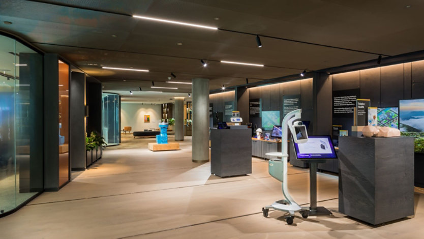 London experience zone - wide shot of an area with dark wood walls, light wood floor, containing demonstration props such as a bright blue industrial pump and a telemedicine machine on casters.