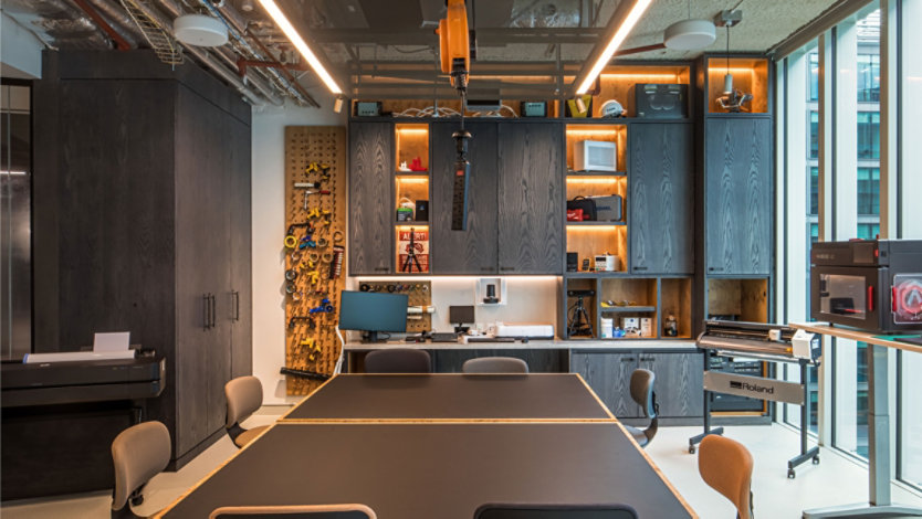 Innovation factory in MTC London.  Dark wood shelving with tools, a pegboard with small equipment.  A 3D printer, wide plotter and cutter.