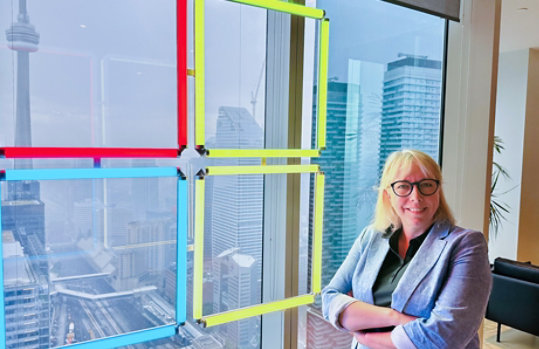 Christine Trudeau of MTC Canada stands beside a window in the Toronto MTC. A Microsoft logo is illuminated through the glass.