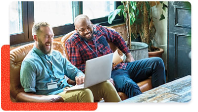 Two people relaxed on couch looking at a laptop and smiling