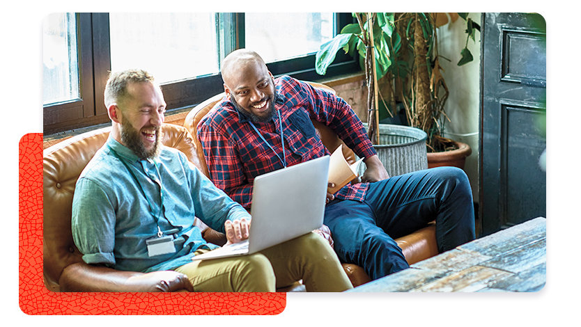 Two people relaxed on couch looking at a laptop and smiling