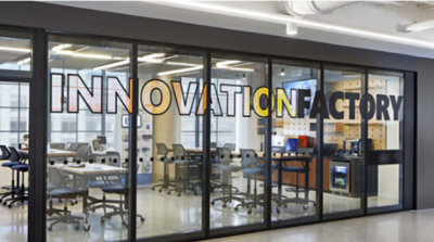 An office with an internal glass wall with large colourful letters spelling Innovation factory