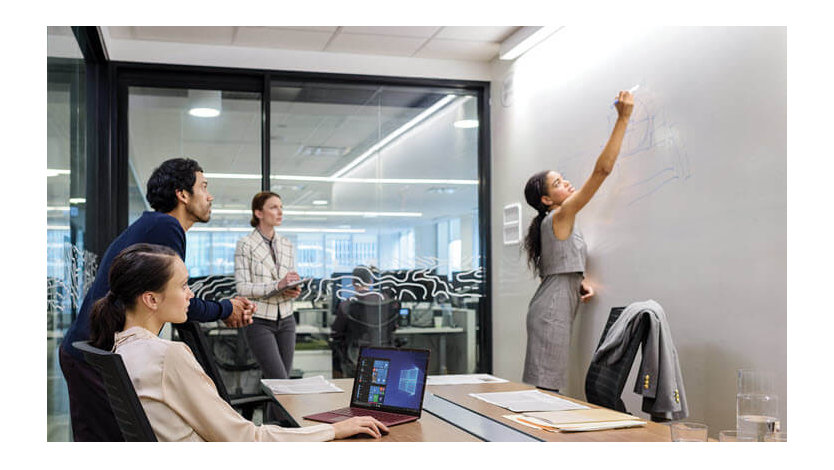 A group of employees in a Microsoft conference room with a person drawing on a white board. 