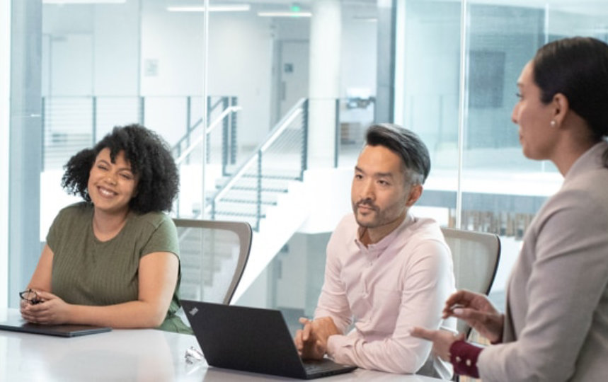 Four businesspeople discussing in a conference room with a slideshow present on the TV.