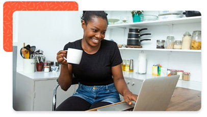 A smiling person sitting behind a laptop, holding a mug