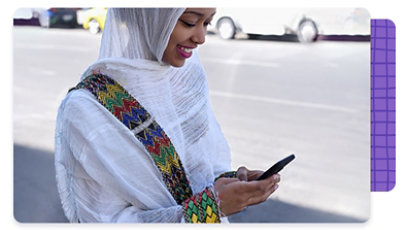 A person wearing a head covering, smiling as they are looking at their mobile phone