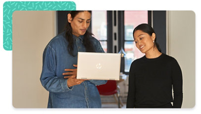 Two colleagues standing next to one another, both looking at a laptop one is holding up