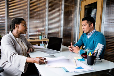 A woman and a man talking in her office with a laptop on the desk.