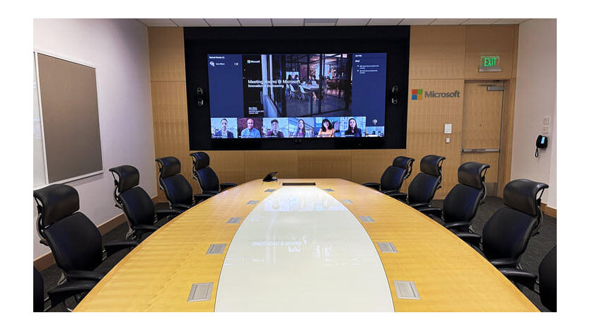 Executives having a discussion in a conference room that’s been updated with the Microsoft Teams Signature boardroom meeting experience.