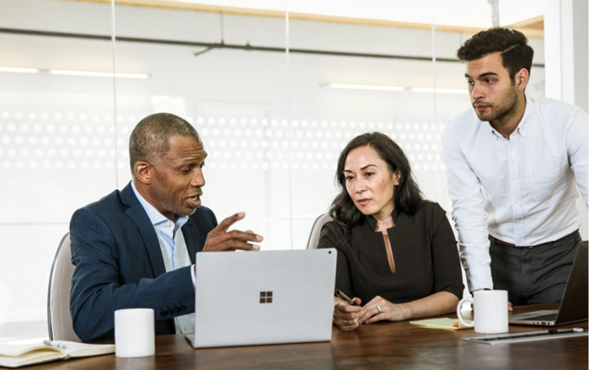Three people in a meeting room talking over a laptop.