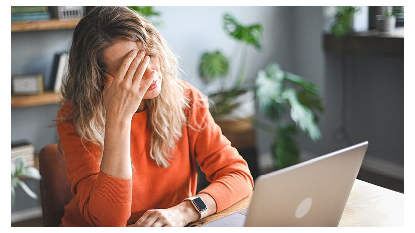 Woman sitting at a desk, with their hand to their head looking stressed