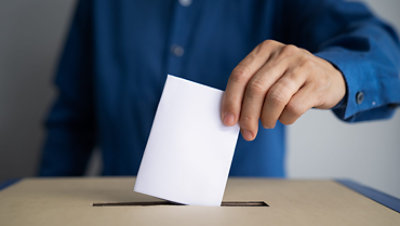 A person drops a vote into a box.