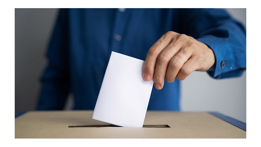 A person drops a vote into a box.