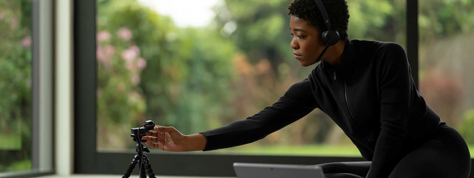 Una mujer que lleva puestos unos audífonos Microsoft Wireless headset ajusta una cámara Microsoft Modern Webcam