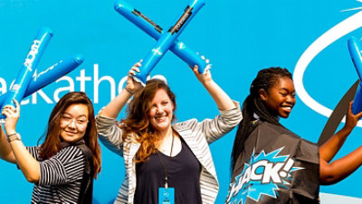 A group of three females celebrate Hackathon and are waving Hackathon swag in the air.