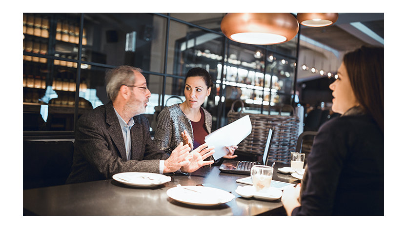 A senior businessman, creative team leader, and female team member having a meeting at a restaurant.