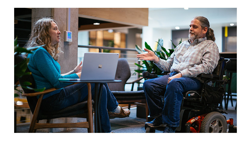 Stuart Pixley, a man who uses a wheelchair, talks to a colleague in the lobby of an office building.