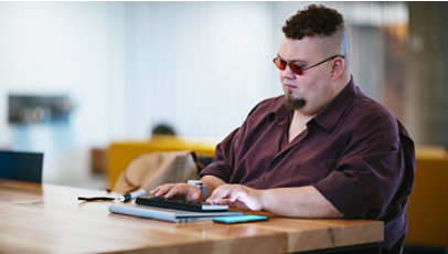 A man who is blind, types on a braille keyboard while also working through a mobile phone.