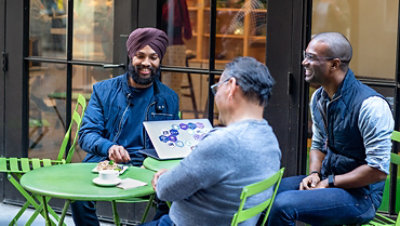 A group of three office workers sit around a table collaborating cheerfully.